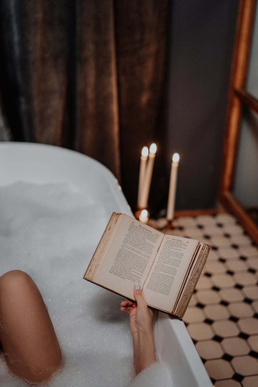 person reading book on white bathtub
