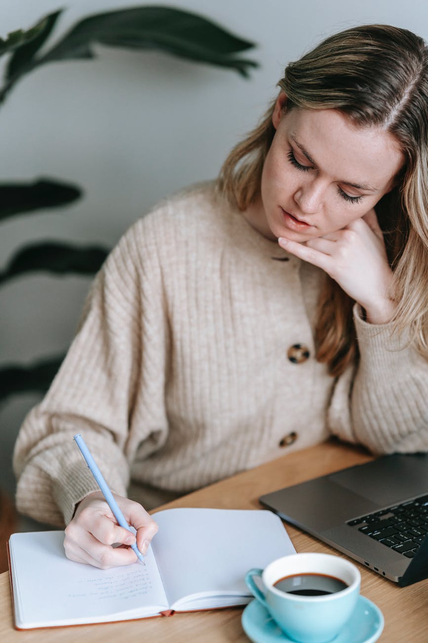 thoughtful woman taking notes in planner near cup of coffee