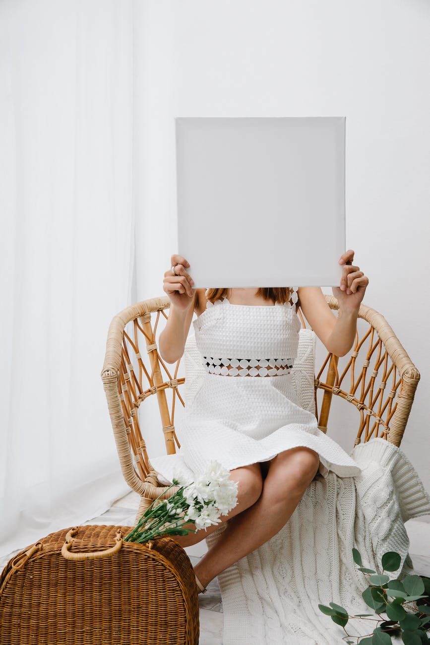 anonymous woman demonstrating blank canvas and sitting on wicker chair